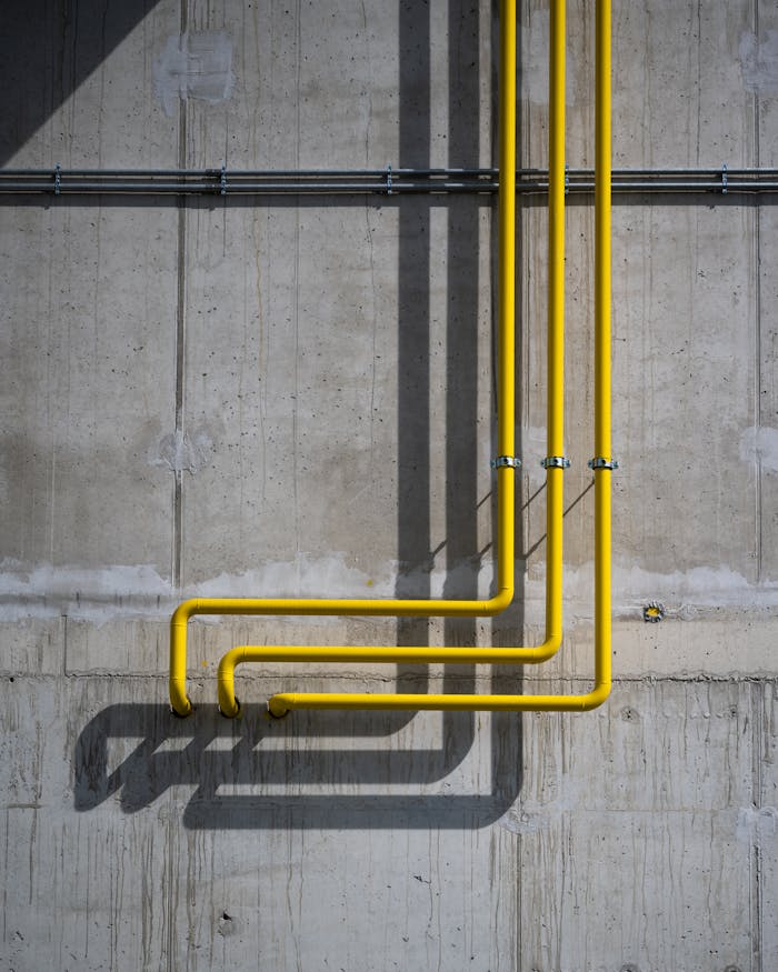 services-06 Vertical yellow pipes casting shadows on a rugged concrete wall in Berlin.