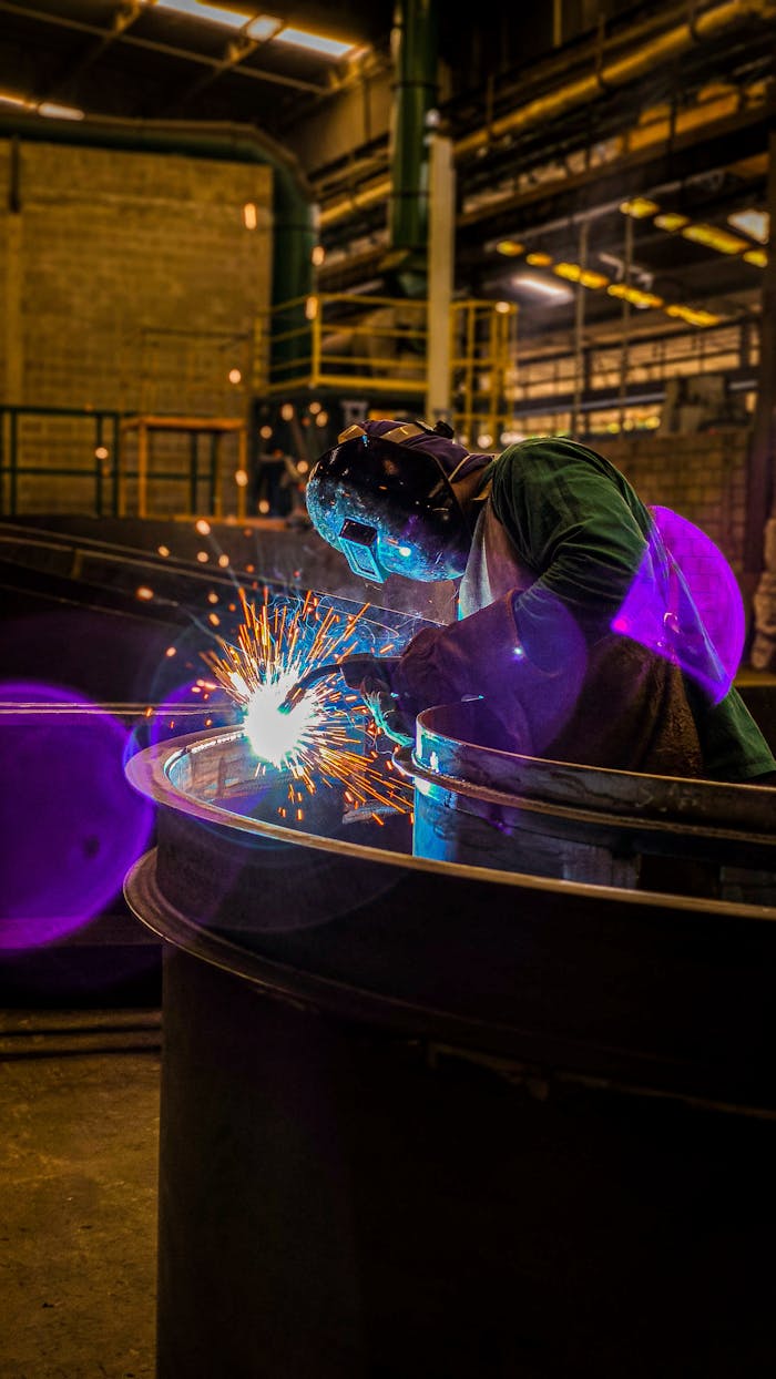 services-05 A skilled welder working with intense sparks in a dimly lit factory setting.